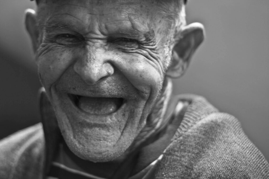 Close-up portrait of an elderly man laughing, capturing a joyful and emotive expression.